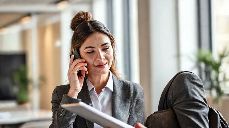 A photorealistic image of a professional travel agent, calm and focused, on a phone call, with a notepad and pen in hand, actively listening. The background is a clean, modern office setting, suggesting professionalism and efficiency. Soft, natural light illuminates the scene, 8K, cinematic lighting, sharp focus, depth of field, professional photography.