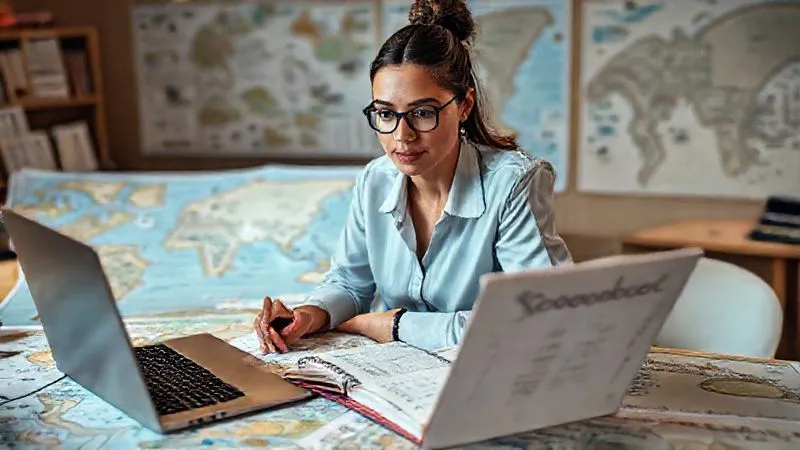 A photorealistic image of a professional woman meticulously planning her international volunteer trip on a large desk, surrounded by maps, a laptop displaying project details, and a notebook with 'Career Goals' written at the top. Cinematic lighting, sharp focus on her determined expression, depth of field blurring the background, 8K hyper-detailed, shot on a high-end DSLR.