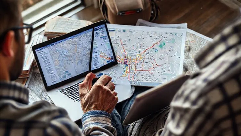 photorealistic, professional photography, 8K, cinematic lighting, sharp focus, depth of field, shot on a high-end DSLR. A traveler meticulously planning their city break on a laptop and tablet, surrounded by guidebooks and printed maps, with a cup of coffee. The screen shows a detailed public transport network map with highlighted routes, conveying a sense of organized preparation and foresight.