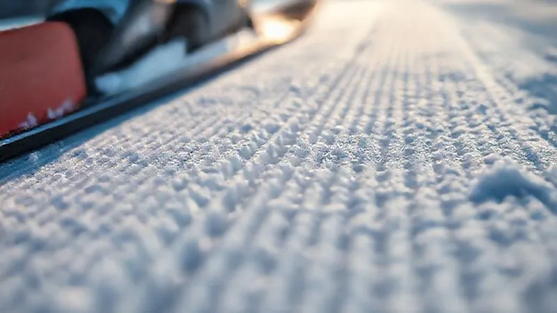 A macro shot, photorealistic, of a cross-country ski base showing a very fine, linear base structure, with tiny, almost invisible grooves. Professional photography, 8K, cinematic lighting, sharp focus on the structure, depth of field, shot on a high-end DSLR.