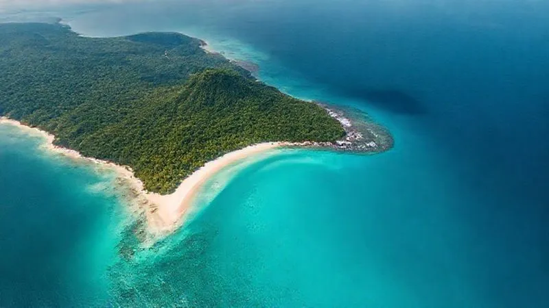 A photorealistic satellite view from high above a remote, undeveloped coastline, showing dense green jungle meeting a crescent of brilliant white sand, with no visible roads or buildings. The water offshore is a gradient of clear turquoise to deep blue, suggesting healthy reefs. 8K, professional photography, sharp focus, depth of field.