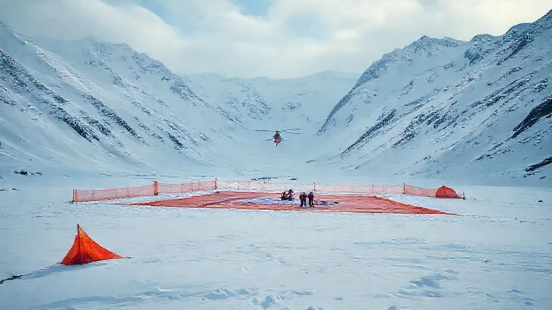 A photorealistic, professional photography, 8K, cinematic lighting, sharp focus, depth of field, shot on a high-end DSLR of a well-marked helicopter landing zone in a vast, snow-covered mountain valley. Bright orange tarps outline the clear area, with a small team standing ready. A rescue helicopter is visible in the distance, approaching the HLZ. The scene conveys readiness and coordination.
