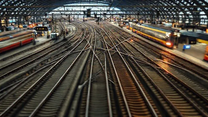 photorealistic, professional photography, 8K, cinematic lighting, sharp focus, depth of field, shot on a high-end DSLR. A complex network of European train tracks converging at a bustling station, with blurred lines of light representing fast-moving trains, symbolizing the intricate and sometimes confusing nature of the European railway system. A digital overlay of reservation symbols and 'X' marks subtly indicates challenges.