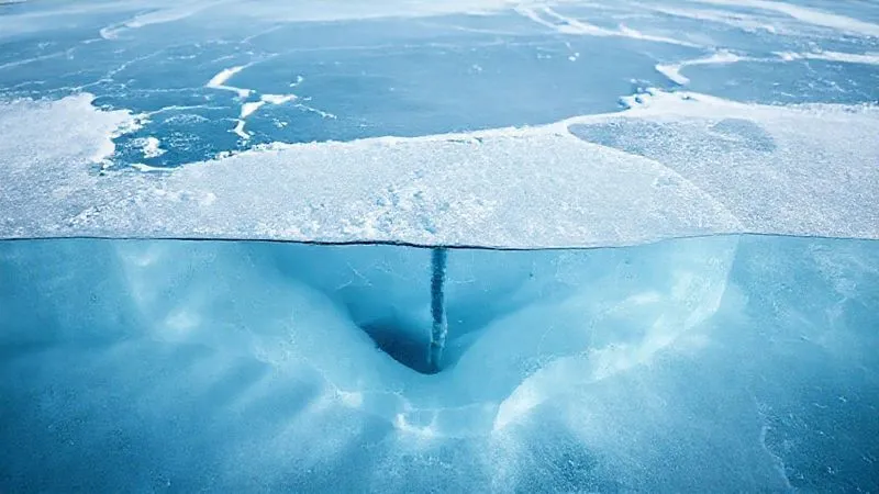 photorealistic, professional photography, 8K, cinematic lighting, sharp focus, depth of field, shot on a high-end DSLR. A cross-section view of a frozen lake, clearly illustrating varying ice thicknesses due to hidden underwater currents, snow cover, and a thermal spring. The ice shows different shades of blue and white, with thin, translucent areas contrasting with thicker, opaque sections. A small ice auger is partially visible, indicating measurement.