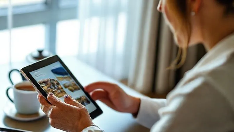 Photorealistic professional photography of an executive thoughtfully using a tablet to research wellness resorts, with a serene, organized workspace and a cup of herbal tea. The screen displays diverse resort options, implying careful consideration and personalized choice. Soft, natural light, sharp focus on the tablet and executive's hands, depth of field blurring the background. 8K hyper-detailed, cinematic lighting.